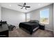 A clean bedroom with a dark comforter, ceiling fan, and two sunny windows at 16528 W Pedro Ln, Goodyear, AZ 85338