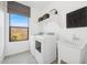 Laundry room with a front-load washer, dryer, utility sink, window, shelf, and gray tile flooring at 7435 S 76Th Dr, Laveen, AZ 85339