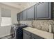 Well-lit laundry room with gray cabinets, floral wallpaper, and modern washer and dryer at 3062 E Cullumber St, Gilbert, AZ 85234