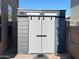 Modern backyard storage shed in gray and white with large doors, surrounded by brick pavers at 17658 N 52Nd Pl, Scottsdale, AZ 85254