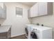 Bright laundry room featuring side-by-side washer and dryer and wall mounted cabinets at 19318 E Reins Rd, Queen Creek, AZ 85142