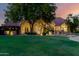 A well-manicured front yard and home featuring a stone facade and mature shade tree at dusk at 2558 E Page Ct, Gilbert, AZ 85234