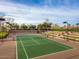An outdoor tennis court is surrounded by trees and greenery under a partly cloudy sky at 29431 N 122Nd Gln, Peoria, AZ 85383