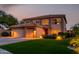 Inviting two-story home featuring lush green grass, a three car garage, and warm exterior lighting at twilight at 9569 W Redbird Rd, Peoria, AZ 85383