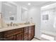 Bathroom featuring dual sinks, dark wood cabinets, marble counters, and a view of the travertine tiled shower at 3919 E Larkspur Dr, Phoenix, AZ 85032