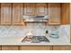 Close up of a kitchen cooktop and vent hood with wooden cabinets and tile backsplash at 7319 E Rose Ln, Scottsdale, AZ 85250