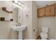Half bathroom with pedestal sink, wood shelves and mirror, and wood cabinet above the toilet at 2511 W Blue Sky Dr, Phoenix, AZ 85085