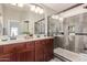Bathroom with double sinks, wood cabinets, and a tiled shower with glass doors at 42022 W Cheyenne Dr, Maricopa, AZ 85138