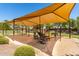 Community playground featuring a large sunshade, multiple swings, and play equipment over sand at 42022 W Cheyenne Dr, Maricopa, AZ 85138