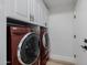 This laundry room features red front load washer and dryer and white cabinets with black and gold pulls at 20437 W White Rock Rd, Buckeye, AZ 85396