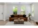 Inviting living room with a leather couch, decorative rug, and plenty of natural light from the two windows at 20437 W White Rock Rd, Buckeye, AZ 85396