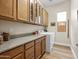 Functional laundry room with ample counter space, wood cabinetry, and a front-loading washing machine near a window at 30287 N 115Th Dr, Peoria, AZ 85383