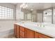 Bathroom featuring double sinks, wood cabinets, tub, shower with glass surround, and a decorative window at 13617 W Crocus Dr, Surprise, AZ 85379