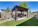 Pergola with sofa swing, dining table, and grill, surrounded by well-manicured backyard landscaping and an artificial lawn at 31332 N 137Th Ln, Peoria, AZ 85383