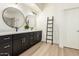 Modern bathroom with dual sinks, black vanity, round mirrors, ladder for towel storage, and light wood floors at 27713 N 57Th Dr, Phoenix, AZ 85083