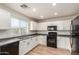 Well-lit kitchen with white cabinets, black appliances, gray countertops, and wood-look flooring at 41251 W Cahill Dr, Maricopa, AZ 85138
