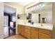Bathroom featuring double sinks, vanity with cabinets, large mirrors and entry to bedroom with hardwood floors at 10786 W Chisholm Dr, Sun City, AZ 85373