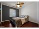Cozy bedroom with dark hardwood floors, neutral tones, a ceiling fan, and a large window with blinds at 10786 W Chisholm Dr, Sun City, AZ 85373