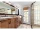 Well-lit bathroom featuring dual sinks, wood cabinets, travertine floors, and a glass block shower at 6417 E Kings Ave, Scottsdale, AZ 85254