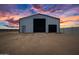 Steel constructed storage building with roll up doors, perfect for equipment or RV storage, with a sunset background at 11564 E Windsor Way, Florence, AZ 85132