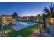 Beautiful backyard with a sparkling pool, outdoor kitchen, seating area and desert landscaping at dusk at 17018 W Saguaro Park Ln, Surprise, AZ 85387
