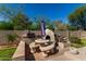 Outdoor kitchen with a pizza oven, grill, stone countertop, and picnic table surrounded by lush green landscaping at 4010 E Hamblin Dr, Phoenix, AZ 85050