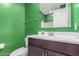 Bathroom with a dark vanity, commode and an eye-catching green accent wall at 17352 W Red Fox Rd, Surprise, AZ 85387