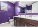 Bathroom with dual sinks, dark vanity, and a bold, purple accent wall at 17352 W Red Fox Rd, Surprise, AZ 85387