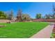 Expansive backyard featuring lush green grass, mature trees, and a charming brick-lined walkway and firepit at 20277 N 68Th Dr, Glendale, AZ 85308