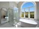 Bright bathroom featuring a soaking tub, glass shower, and a large arched window overlooking mature greenery at 12222 N 74Th St, Scottsdale, AZ 85260