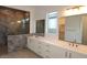 Bathroom boasting dual vanities with white cabinetry, a marble shower, and a window at 12323 W Luxton Ln, Avondale, AZ 85323