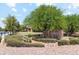 Community entrance sign surrounded by desert landscaping, mature trees, and a glimpse of the community buildings at 8516 W Clemente Way, Florence, AZ 85132