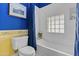 Bright bathroom featuring a tub with a shower, blue walls, a toilet, and unique glass block window at 11439 E Bella Vista St, Scottsdale, AZ 85259
