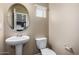 A well-lit powder room features a pedestal sink, round mirror, and toilet, offering convenience for guests at 240 W Juniper Ave # 1211, Gilbert, AZ 85233