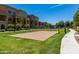 Community sand volleyball court surrounded by green grass, sidewalks, and multi-story townhomes on a sunny day at 240 W Juniper Ave # 1211, Gilbert, AZ 85233