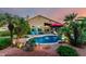 Inviting backyard featuring a sparkling pool, mature palm trees, vibrant plants, and ambient lighting for evening enjoyment at 2058 E Marlene Dr, Gilbert, AZ 85296
