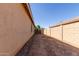 Side view of a tan home showcasing a dirt backyard with a metal gate at 40027 W Pryor Ln, Maricopa, AZ 85138
