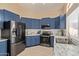 Modern kitchen features stainless steel appliances, granite countertops, tile backsplash and beautiful blue cabinetry at 5018 W Wikieup Ln, Glendale, AZ 85308