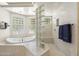 Sunlit main bathroom with a glass block shower, soaking tub, and neutral tile floors at 3146 E Maryland Ave, Phoenix, AZ 85016