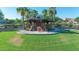 A park gazebo is surrounded by green grass, mature trees, and comfortable seating at 10650 E Palladium Dr, Mesa, AZ 85212