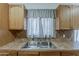 Kitchen sink with wood cabinets, tile backsplash, stainless steel sink, and a window with drapes at 3347 W Roma Ave, Phoenix, AZ 85017