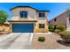 Two-story home featuring a blue garage door, desert landscaping, and an American flag displayed out front at 40316 W Hopper Dr, Maricopa, AZ 85138