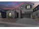 Exterior view of a two-story home with a gray stucco, arched window, and two-car garage during a sunset at 21276 W Mariposa St, Buckeye, AZ 85396