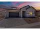 Beautiful single-story home featuring stucco and stone exterior and a paved driveway under a colorful sunset sky at 21427 W Meadowbrook Ave, Buckeye, AZ 85396