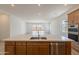 Kitchen island with sink, wood cabinets, stainless steel dishwasher, and views of the bright living room at 21427 W Meadowbrook Ave, Buckeye, AZ 85396