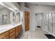 Well-lit bathroom with double sinks, wooden cabinetry, and a glass-enclosed shower at 18066 W Weatherby Dr, Surprise, AZ 85374