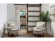 Bedroom sitting area with two armchairs, modern barn door to bathroom, wood flooring, and light, neutral decor at 8708 E Rancho Vista Dr, Scottsdale, AZ 85251