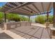 Outdoor kitchen with built-in grill and bar seating under a pergola, surrounded by lush landscaping and mature trees at 1063 W Vaughn St, Tempe, AZ 85283