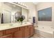 Bathroom featuring a dual sink vanity, soaking tub, large mirror, and natural light at 16288 W Hadley St, Goodyear, AZ 85338