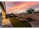 Landscaped backyard with a water feature, synthetic grass, and outdoor lounge chair under a vibrant sunset sky at 17812 W Primrose W Ln, Surprise, AZ 85374